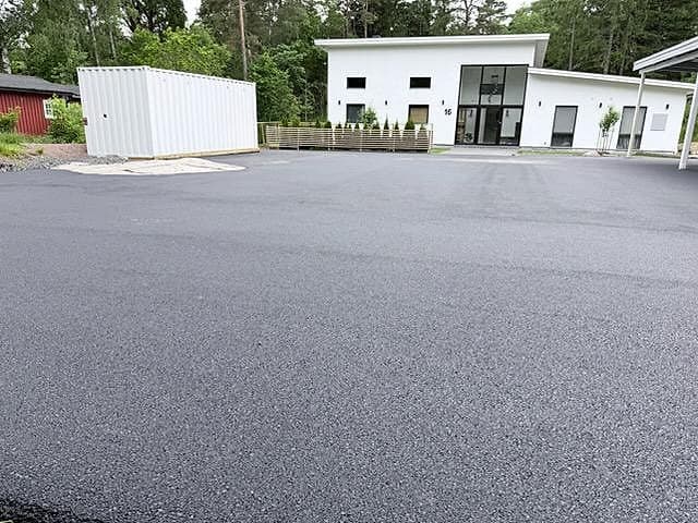 Nyasfalterad gårdsplan framför ett vitt hus.